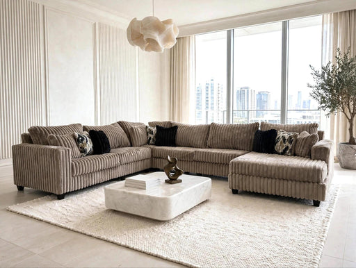 A modern L-shaped sectional sofa upholstered in taupe corduroy fabric, styled in a bright, contemporary living room with a white marble coffee table and a large white textured area rug.
